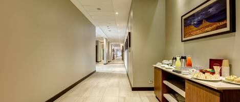 A hotel corridor with a reception desk, a painting, and a long hallway.