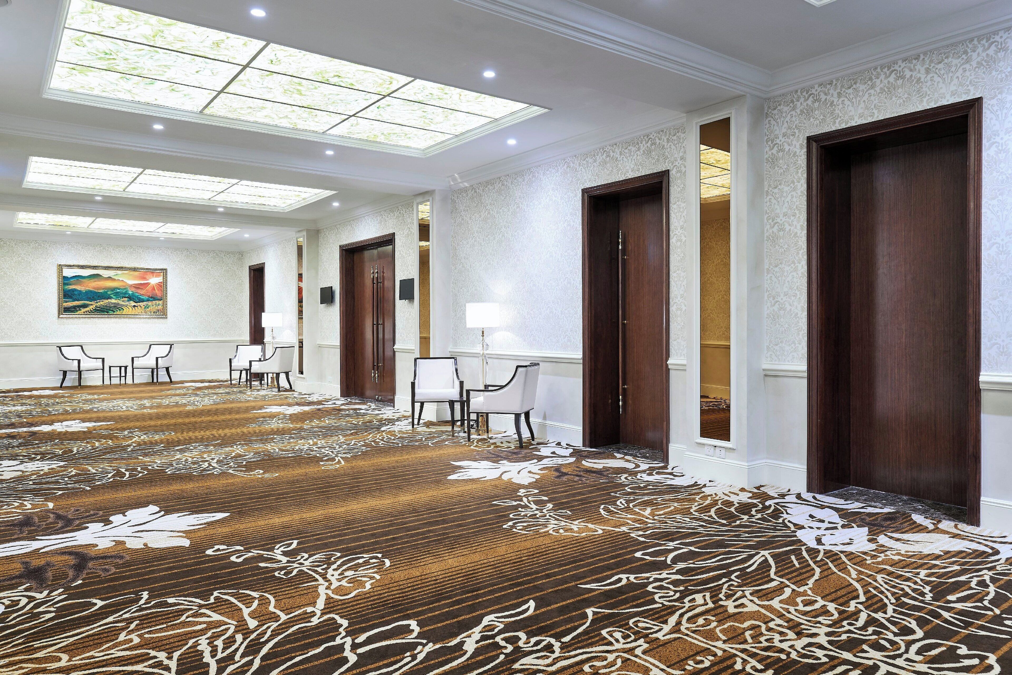 Un hall d’hôtel spacieux, doté d’un tapis à motifs, de portes en bois et d’un tableau accroché au mur.