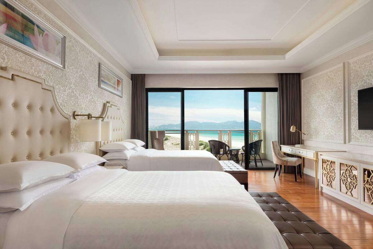 A hotel room with two beds, a desk, and a view of the beach.