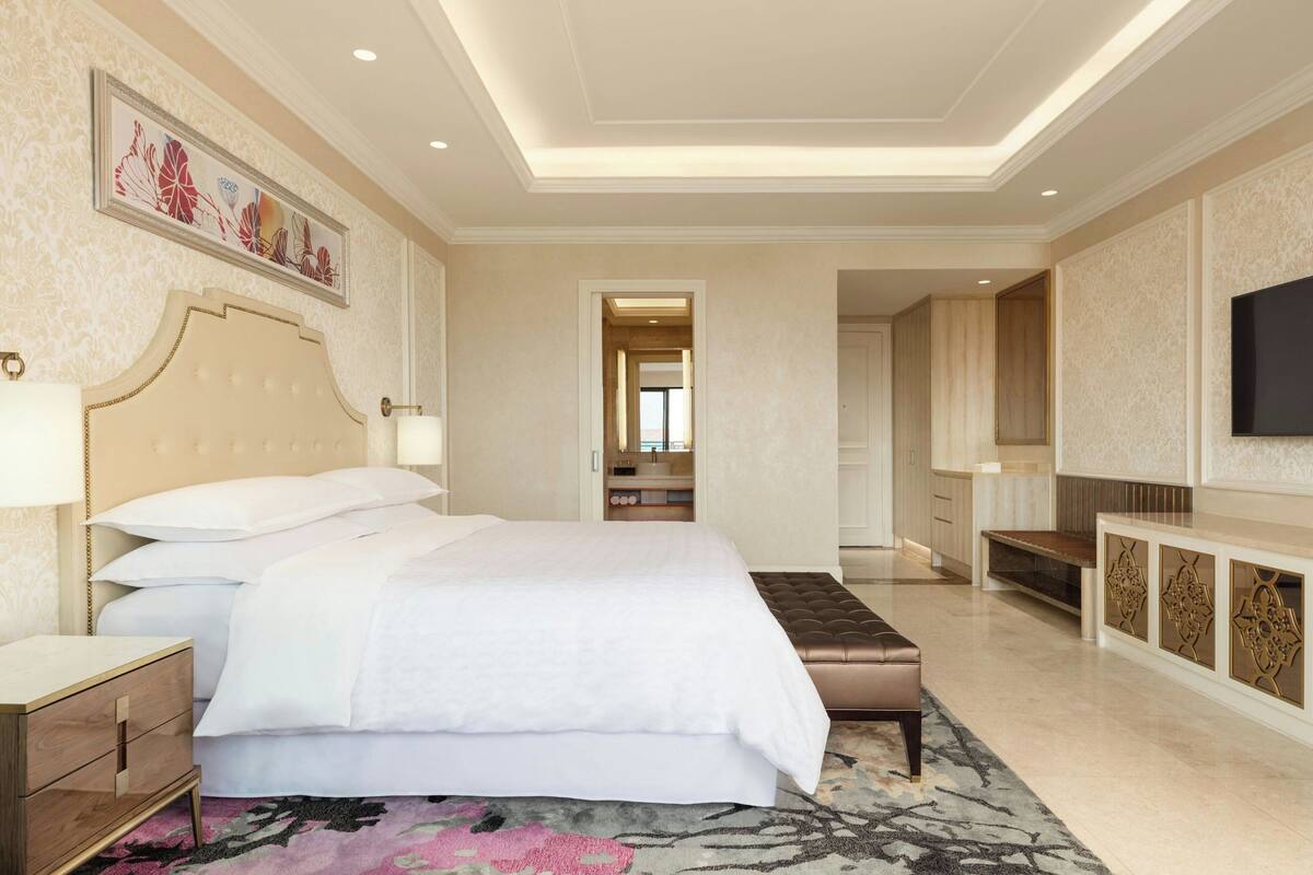 A spacious bedroom with a large bed, bedside tables, a bench, a TV, and a walk-in closet.