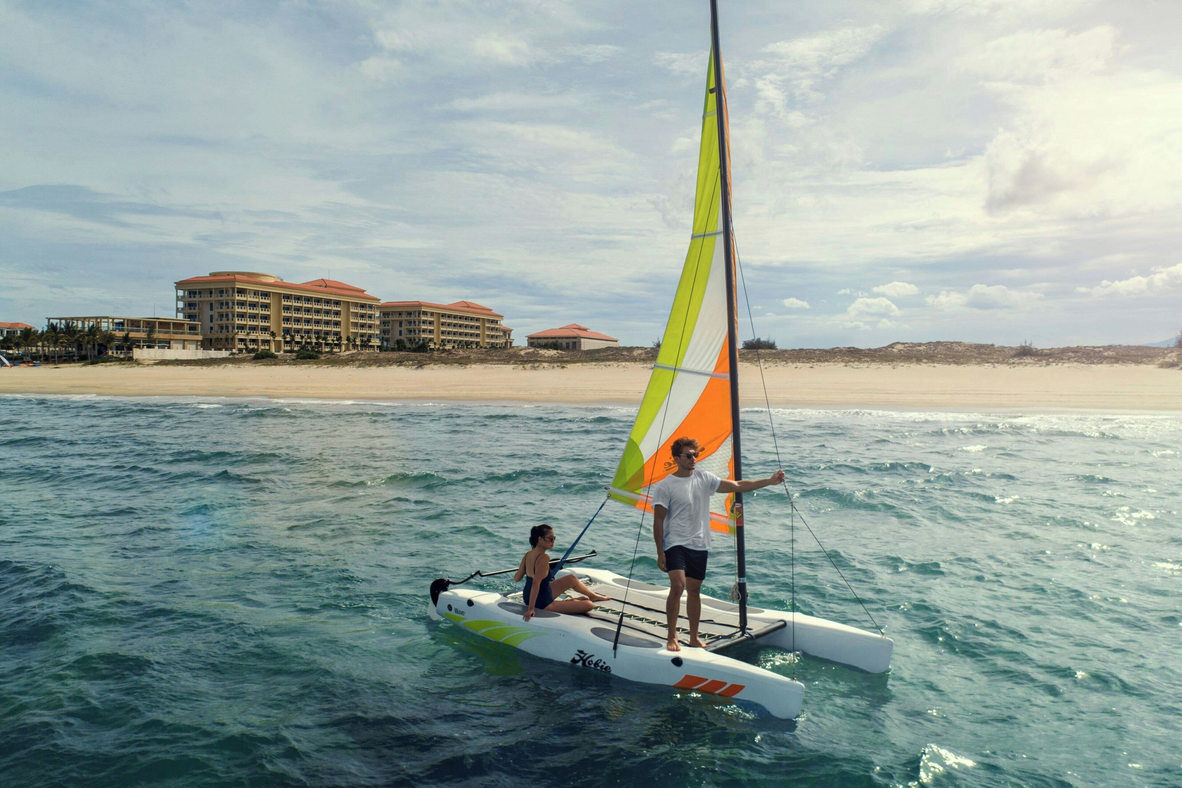 A sailboat on calm waters with a beach and hotel buildings in the background.