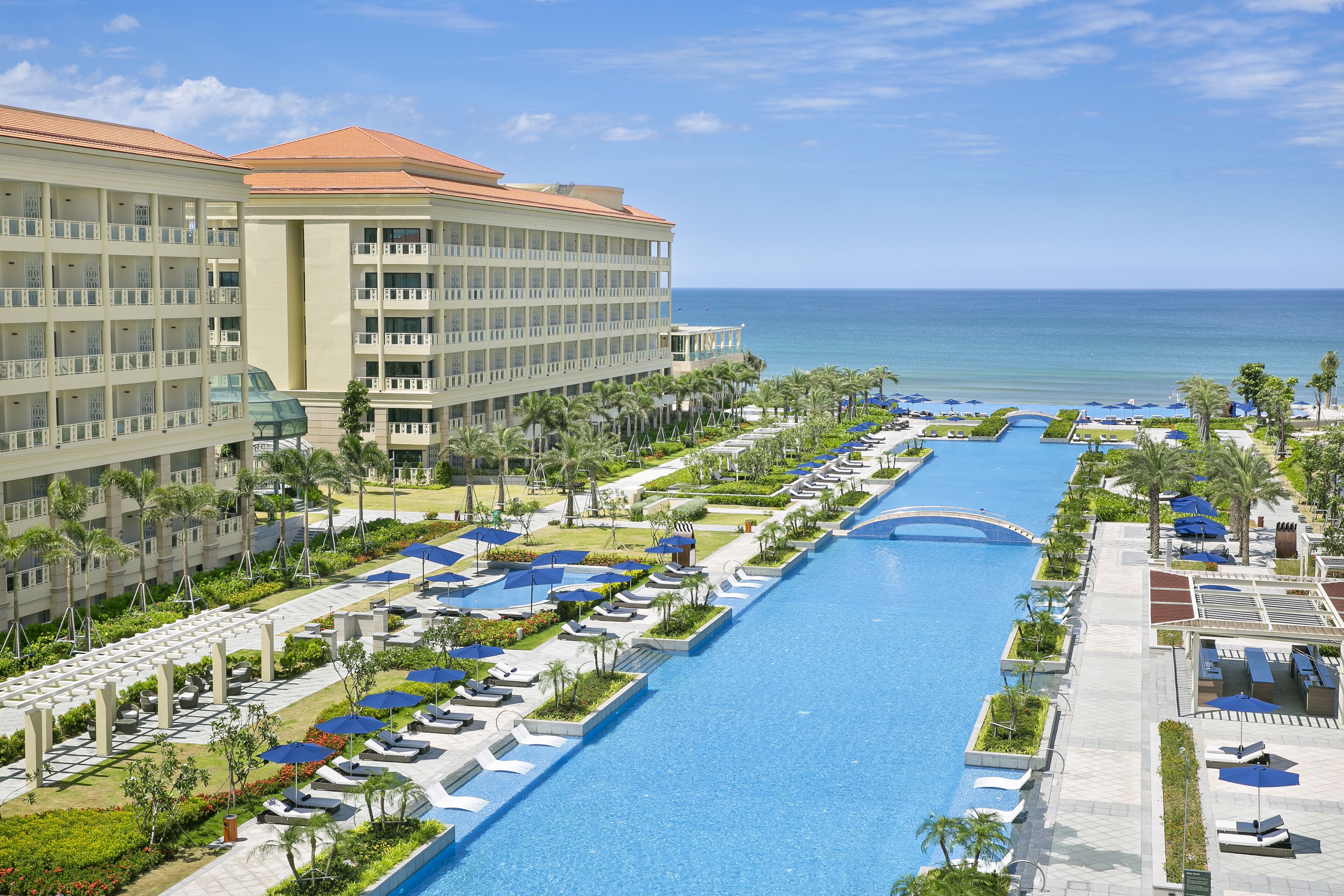 A resort with a long swimming pool, multiple levels of balconies, and a view of the ocean.