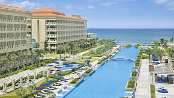 A resort with a long swimming pool, multiple levels of balconies, and a view of the ocean.