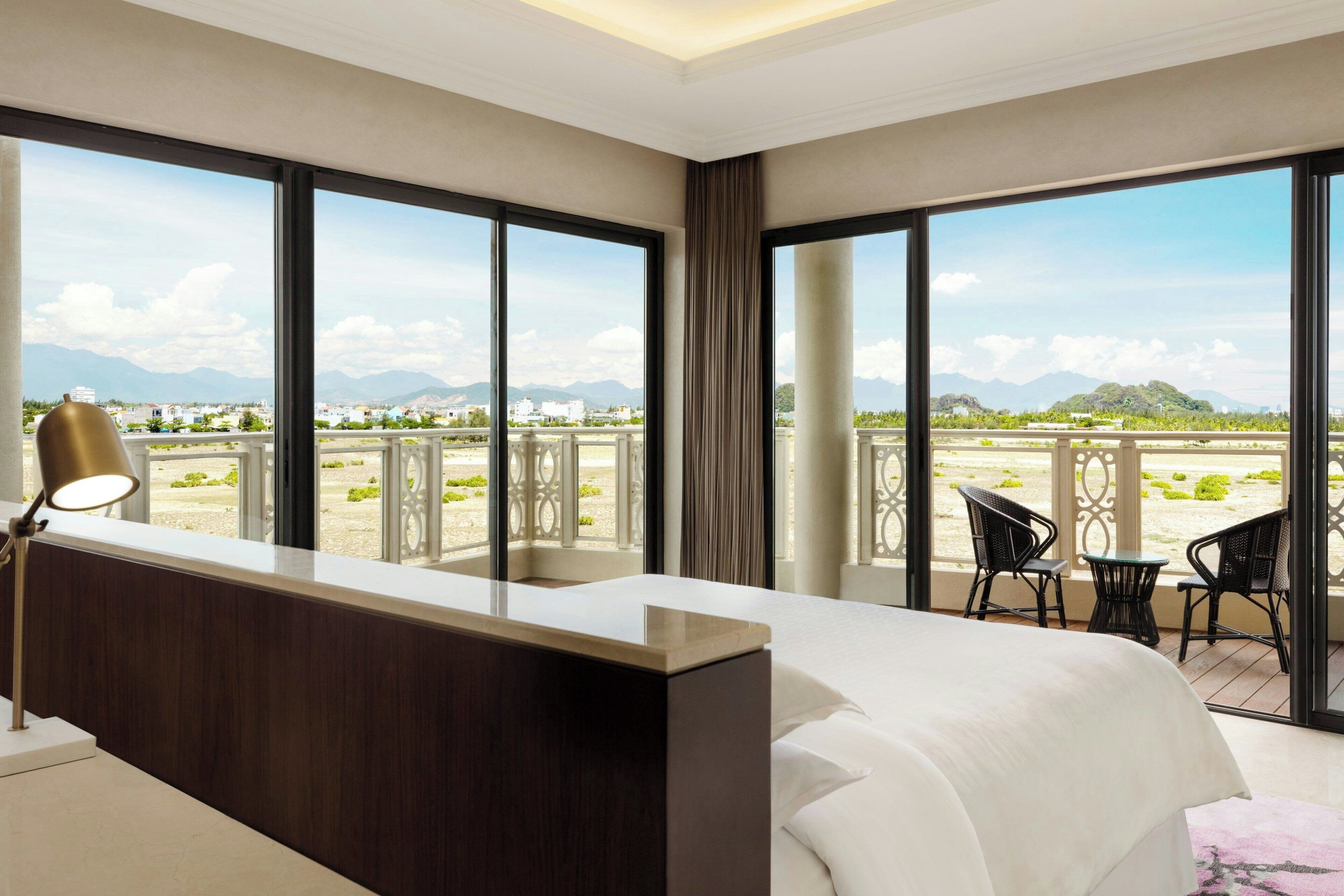 A hotel room with a large bed, a desk, and a balcony with chairs and a table.