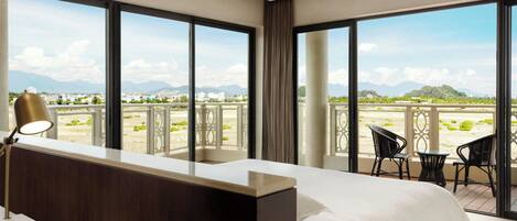 A hotel room with a large bed, a desk, and a balcony with chairs and a table.