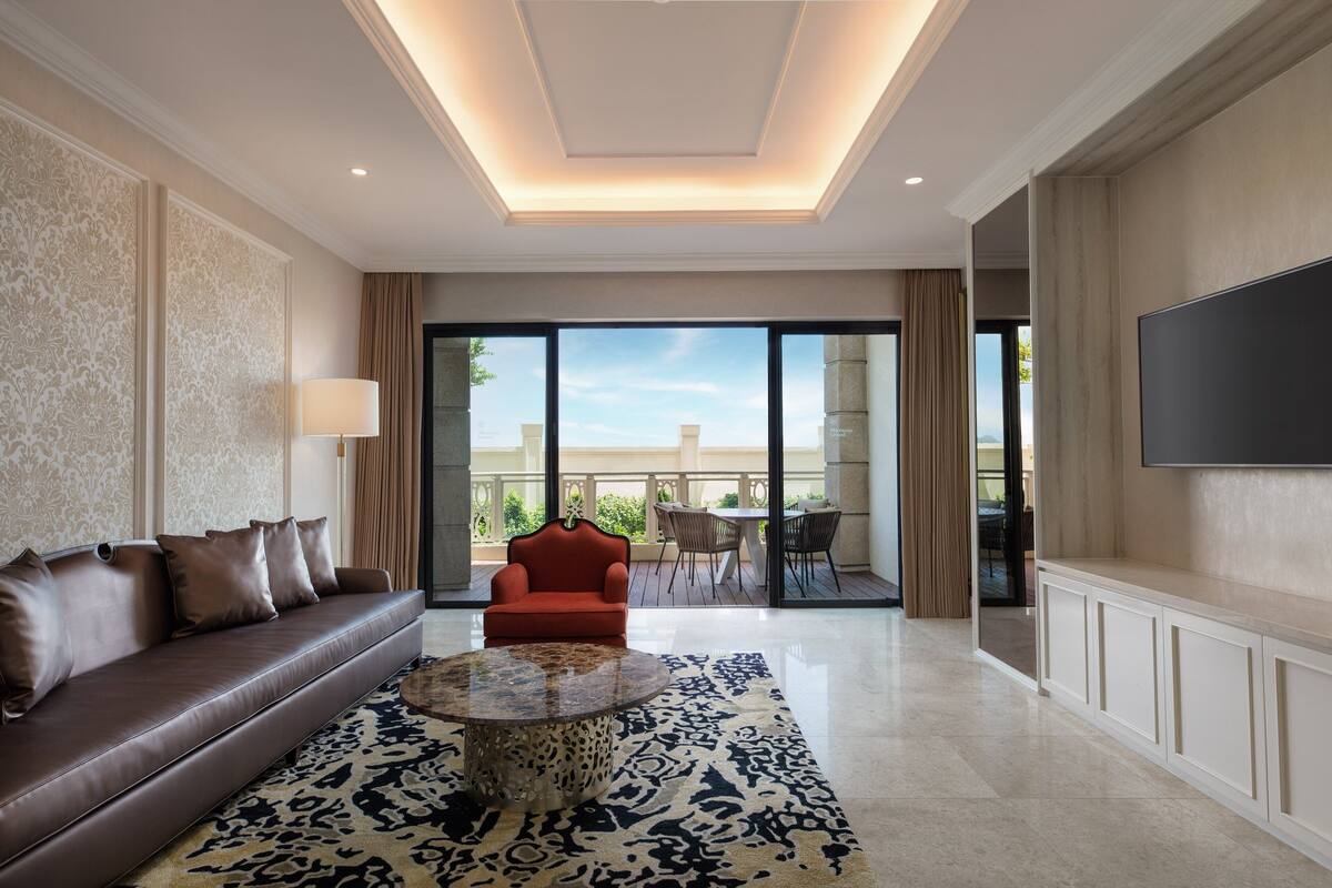 A spacious living room with a brown leather sofa, a red armchair, a patterned rug, and a large flat-screen TV.