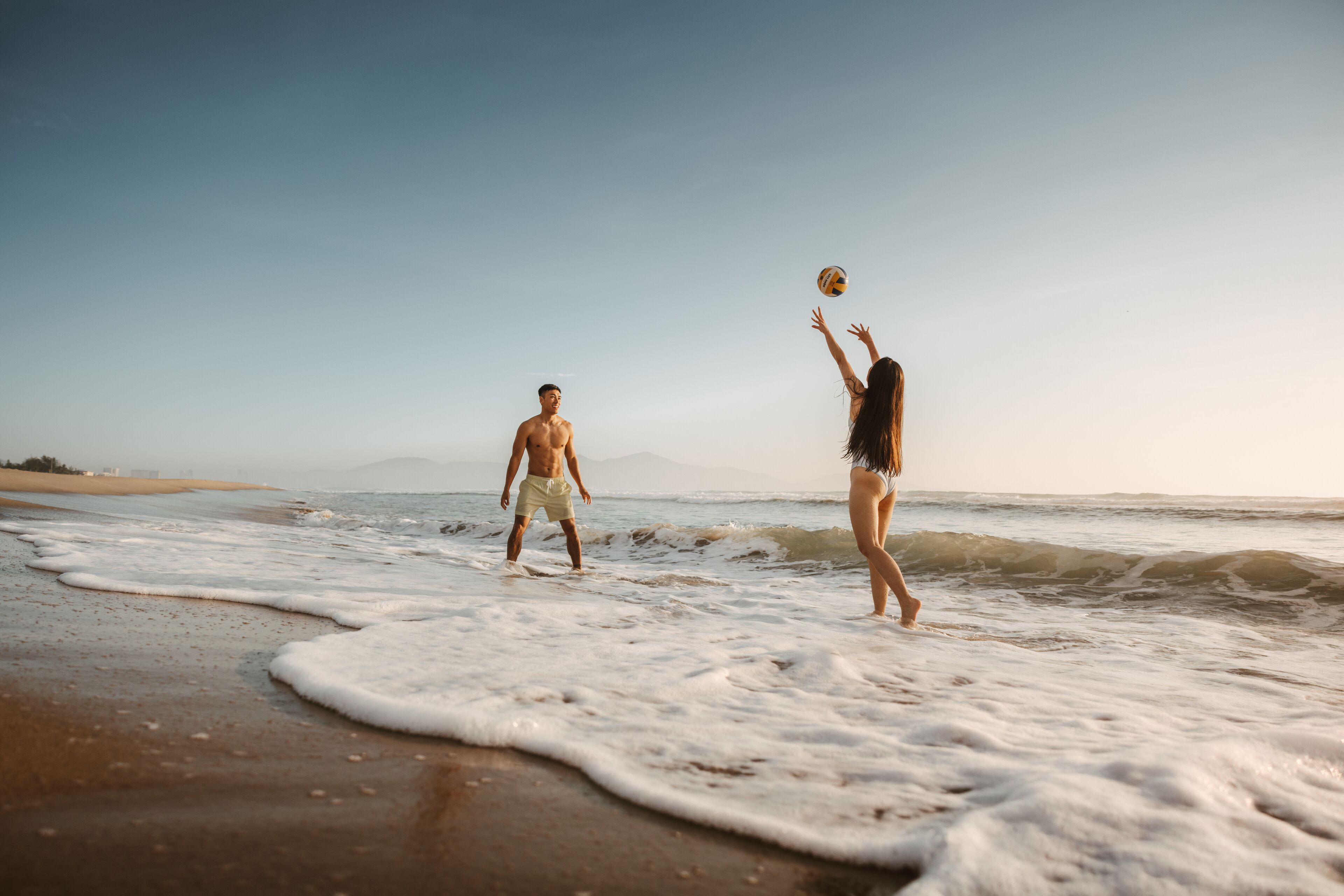 A beach scene with two people playing with a volleyball.