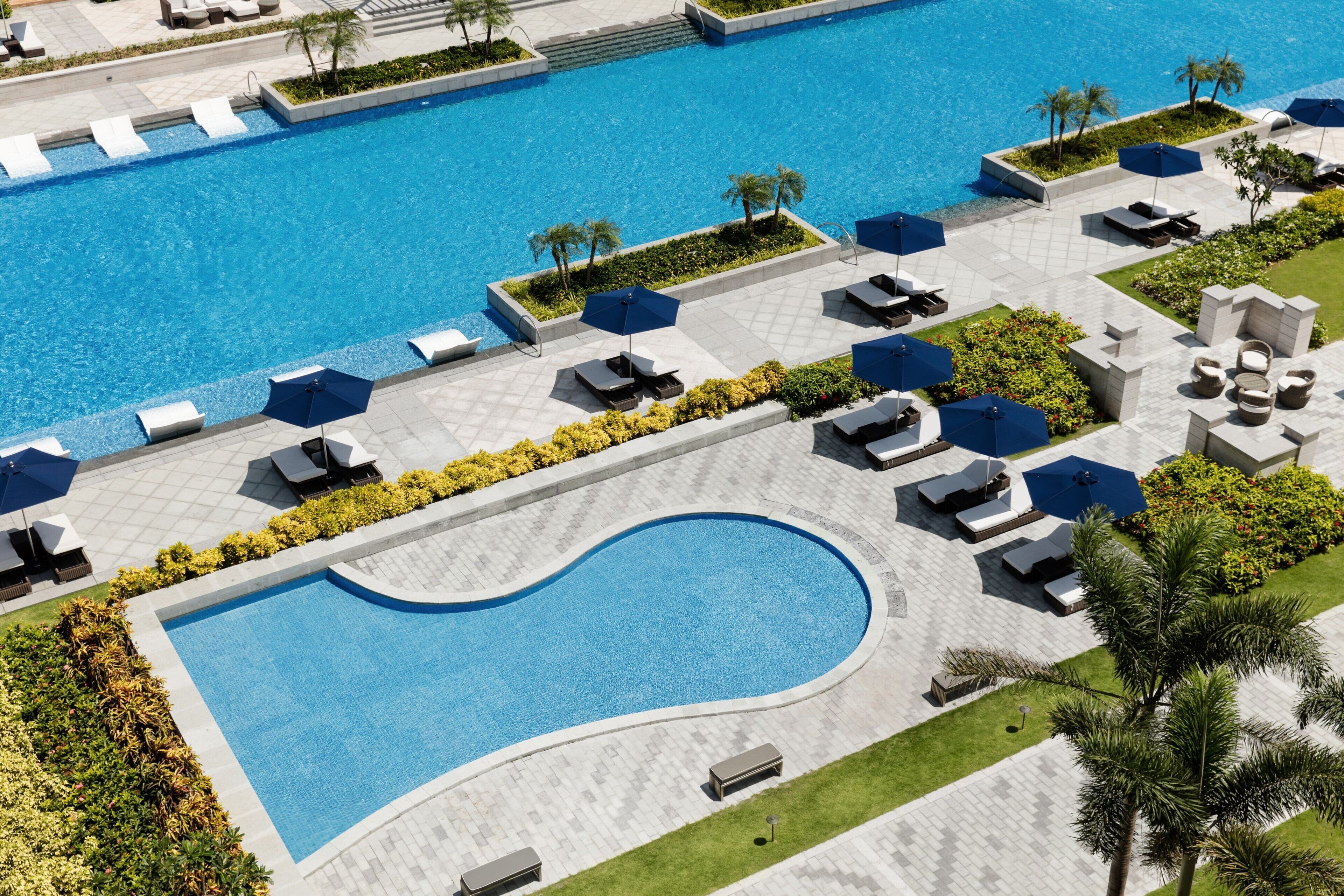 A large swimming pool with multiple lounge areas, sunbeds, and umbrellas.