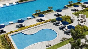A large swimming pool with multiple lounge areas, sunbeds, and umbrellas.