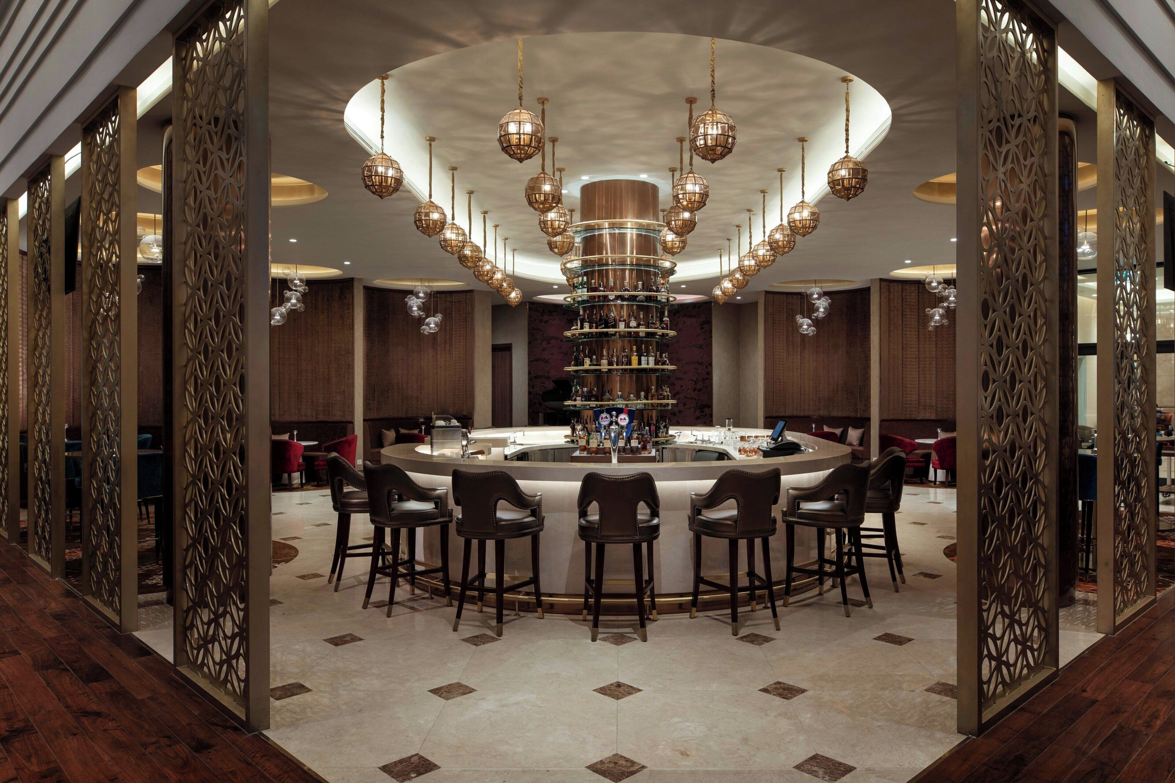 A bar area with a central bar counter, multiple bar stools, and a decorative light fixture above.