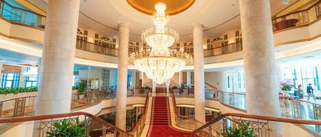 A grand lobby with a central chandelier, multiple floors, and a red carpeted staircase.