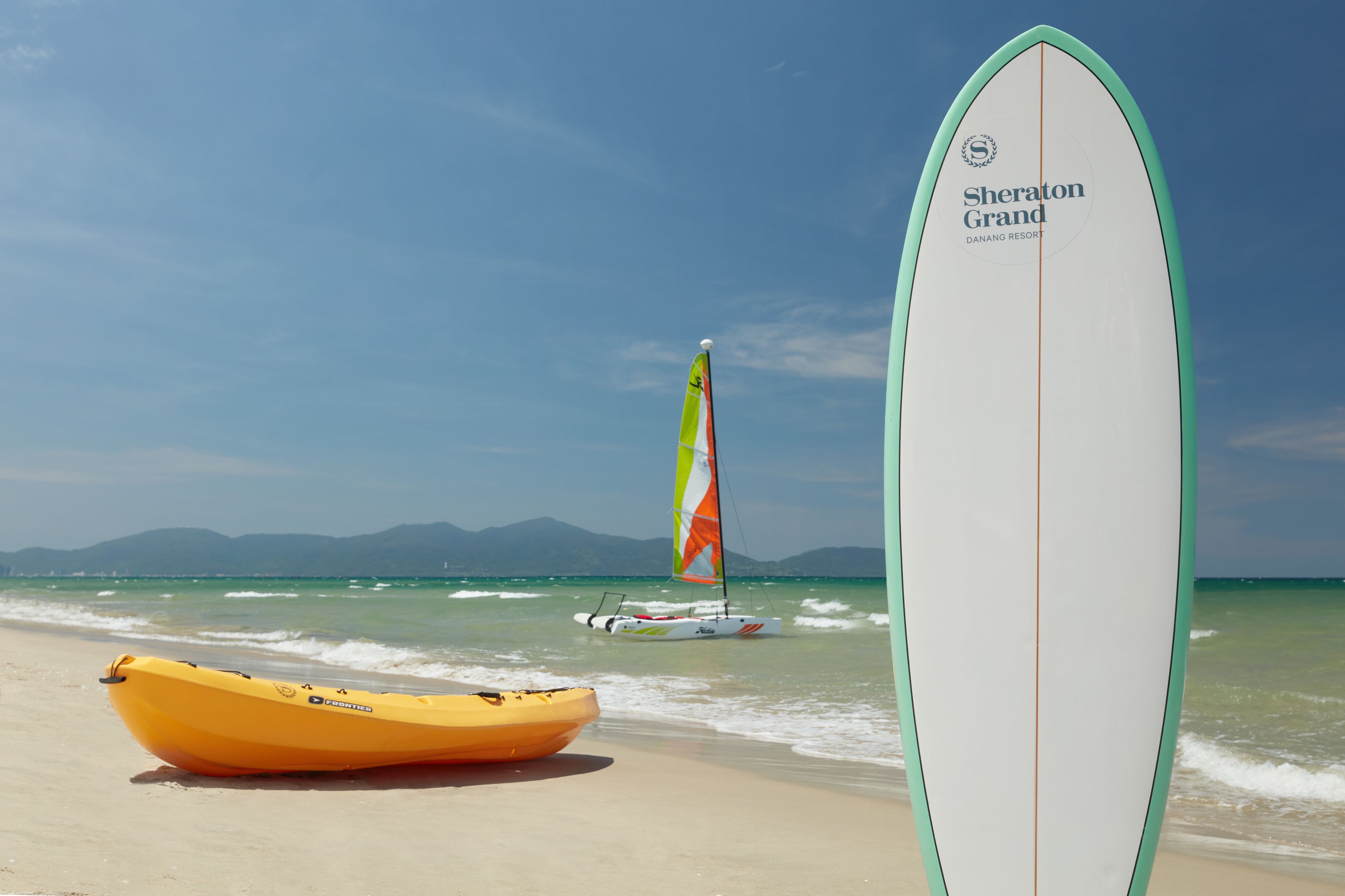 A beach scene with a surfboard, a kayak, and a sailboat.