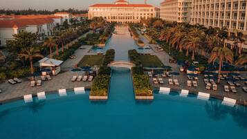 Un hotel grande con piscina central, varias edificaciones y palmeras.