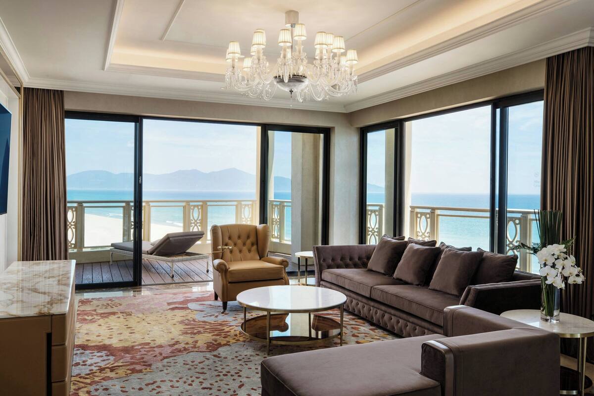 A spacious living room with a large window, a chandelier, a sofa, a chair, and a coffee table.