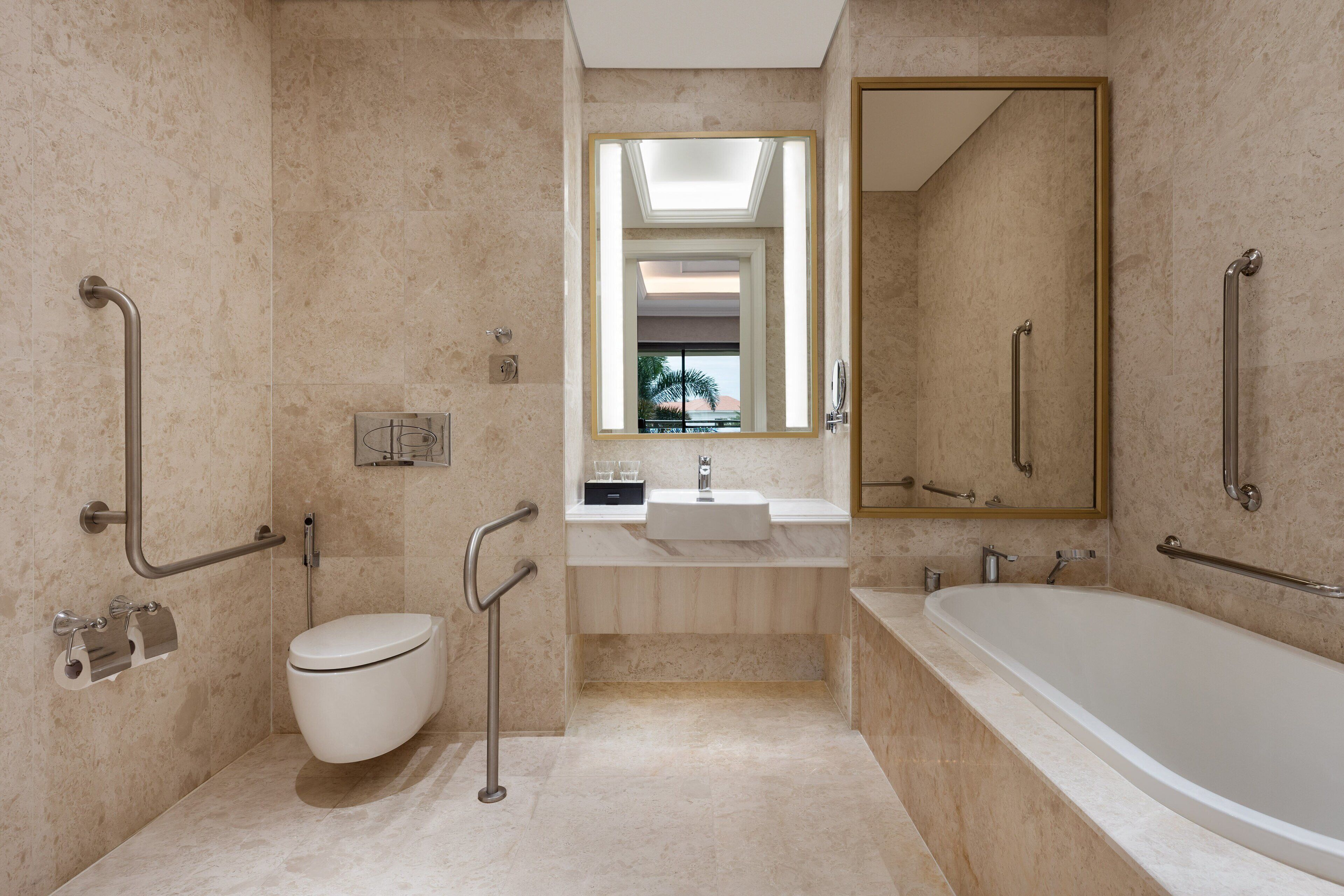 A modern bathroom with a toilet, sink, and bathtub, equipped with grab bars and a mirror.