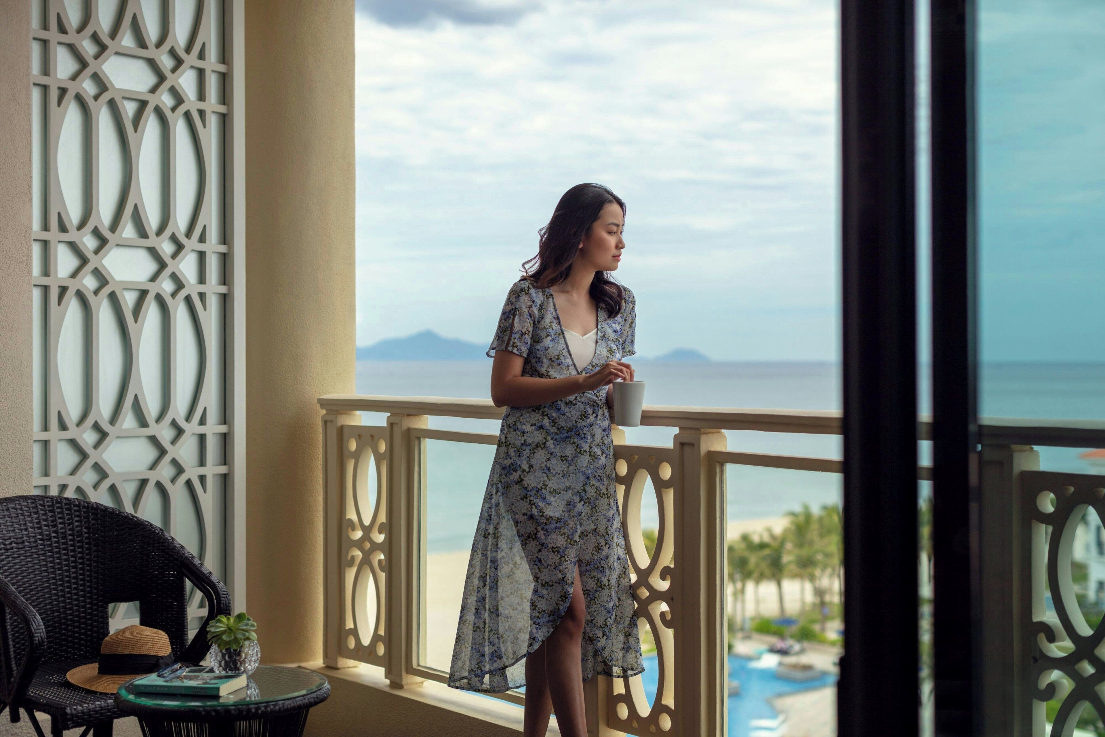 Een vrouw staat op een balkon met uitzicht op de oceaan en een zwembad.