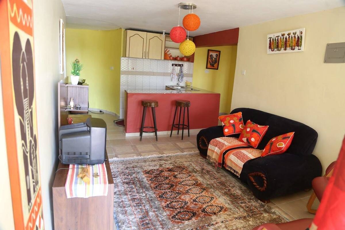 A living room with a sofa, a TV, and a kitchen area with stools.