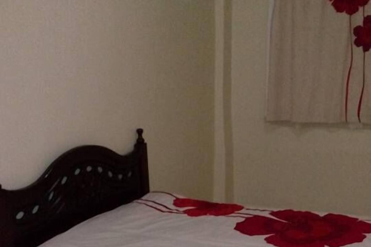 A bedroom with a bed, a red patterned rug, and a wall with a red flower decoration.