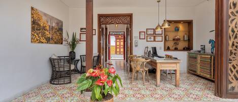 A spacious lobby with a tiled floor, a central potted plant, and a wooden reception desk.
