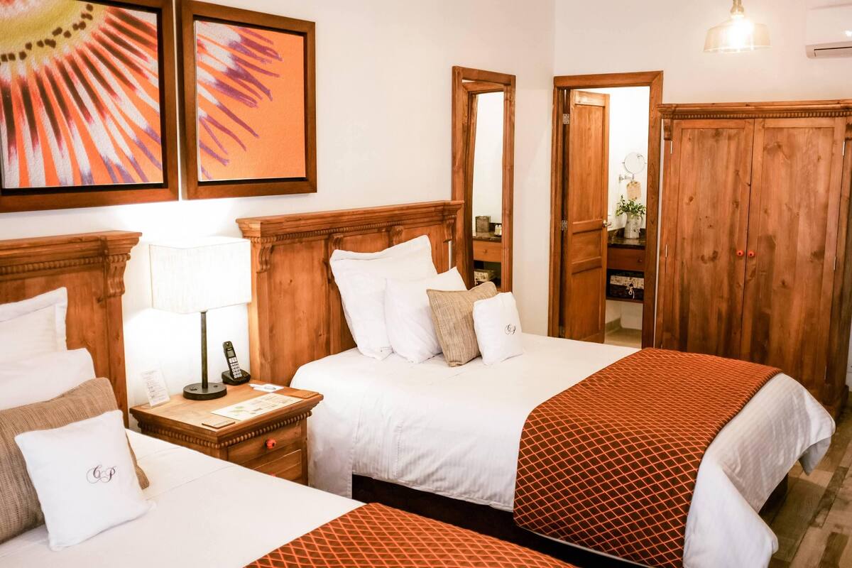 Ein Hotelzimmer mit zwei Betten, Holz-Kopfteilen, einem Nachttisch mit Lampe, einem Spiegel und einem Kleiderschrank.