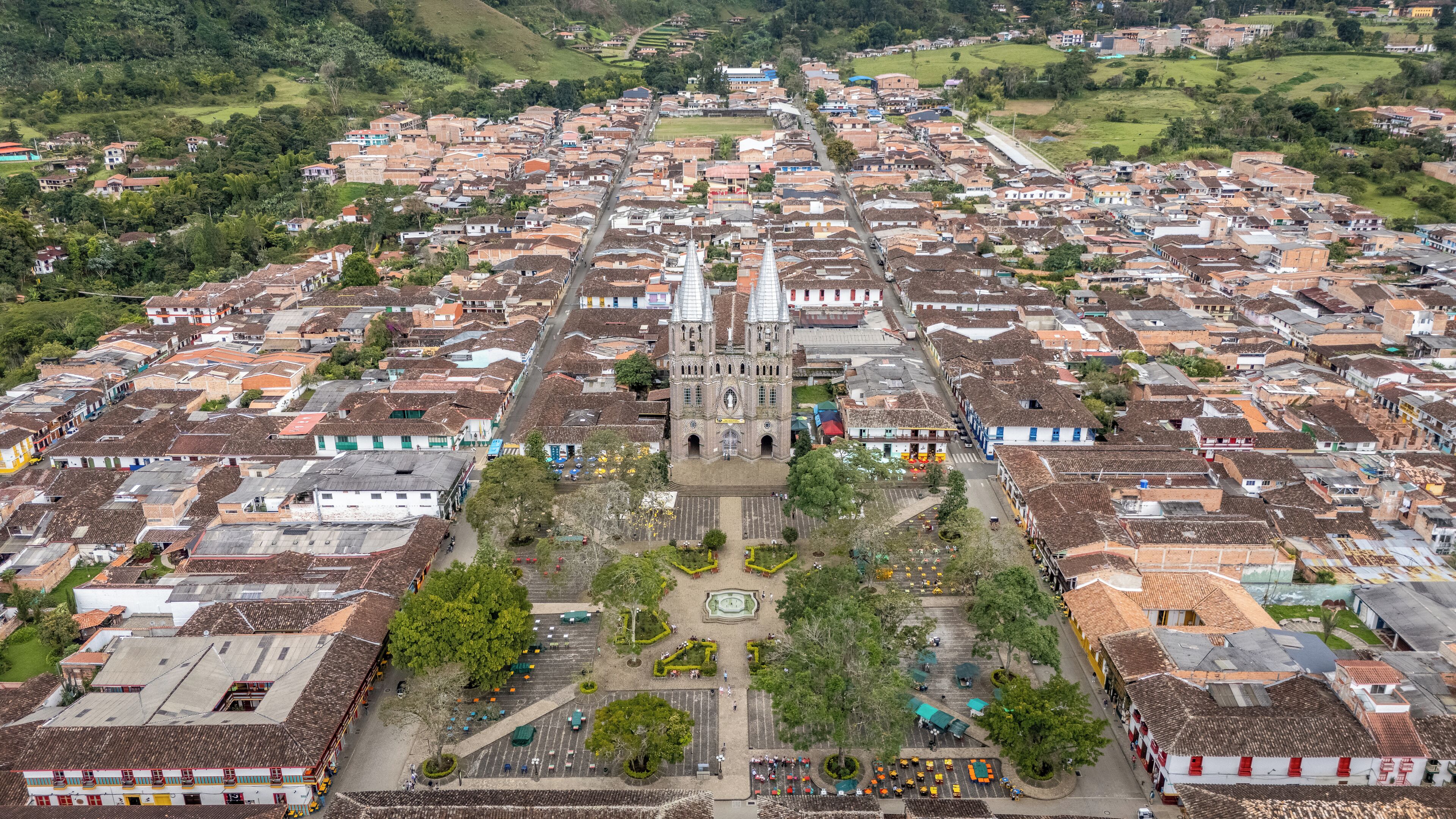 An aerial view of a town with a prominent church in the center, surrounded by residential buildings and a central square with a fountain.