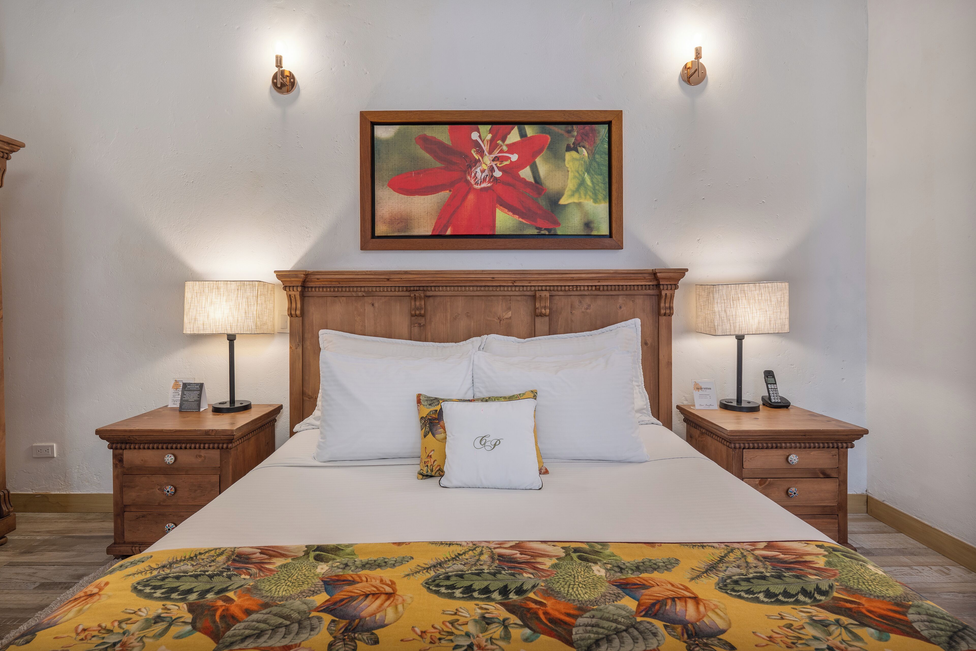 A neatly made bed with white linens, a floral-patterned bedspread, and two bedside tables with lamps and a clock.