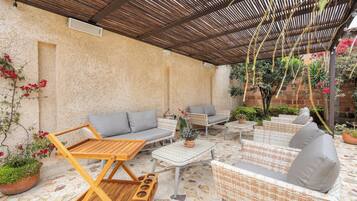A covered outdoor seating area with wicker furniture and a stone floor.