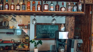 Un espace bar avec des étagères remplies de bouteilles d’alcool, une machine à café et un tableau noir servant de panneau d’affichage.
