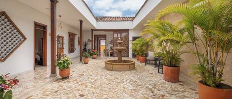 Un patio con una fuente, plantas en macetas y suelo de baldosas.