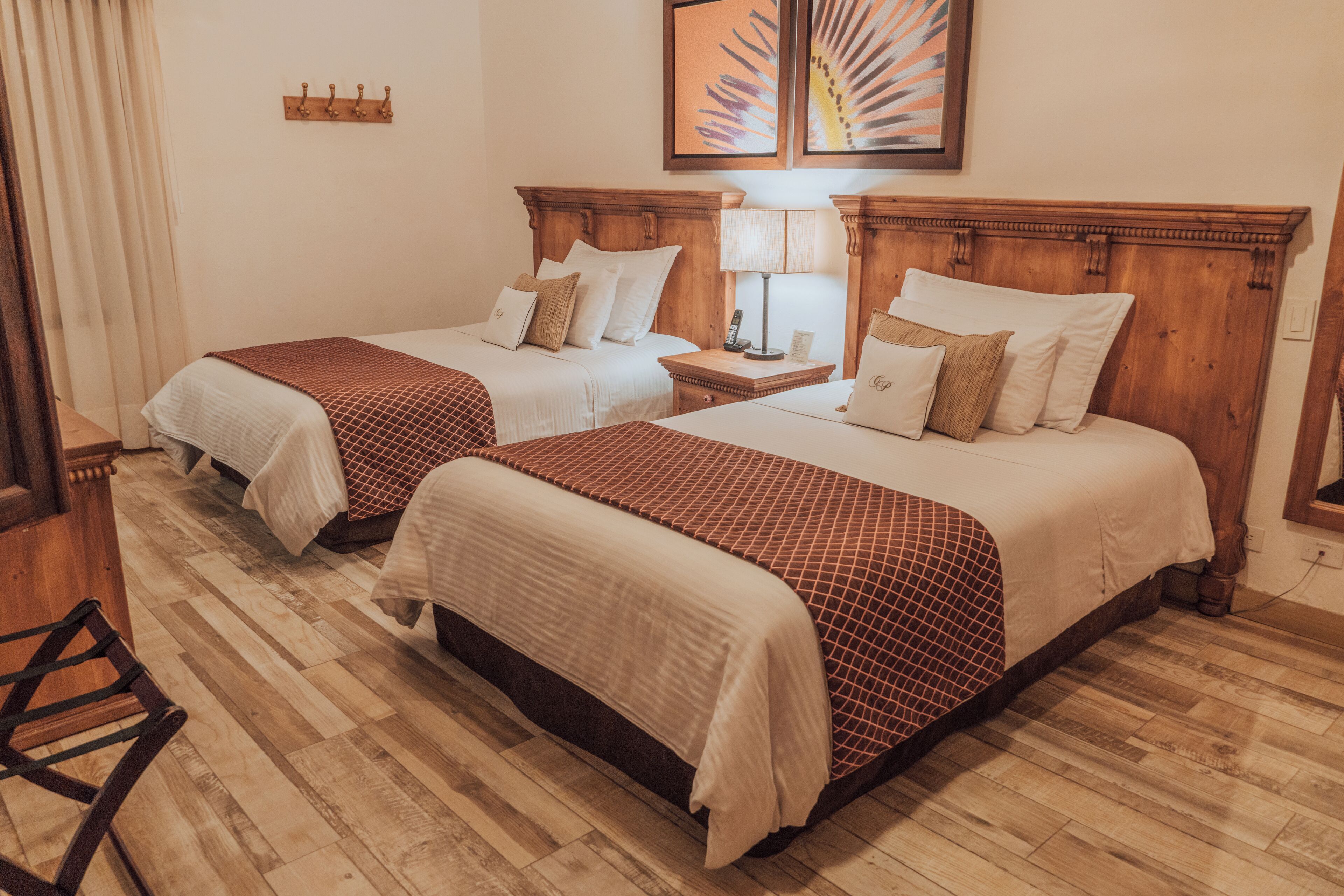 A hotel room with two beds, wooden headboards, a wooden floor, a chair, and artwork on the wall.