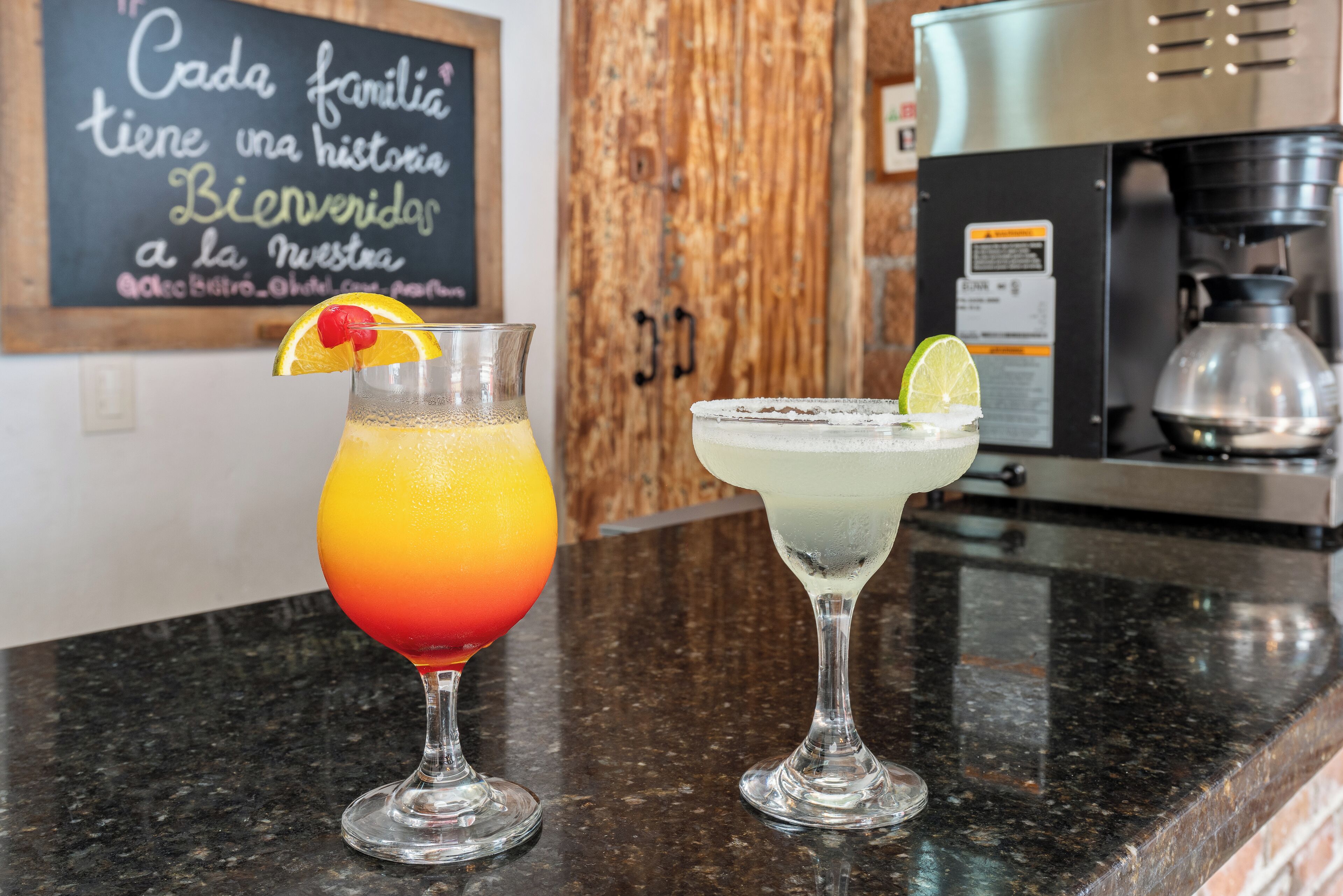 Two cocktails on a kitchen counter with a coffee machine and a wooden cabinet in the background.