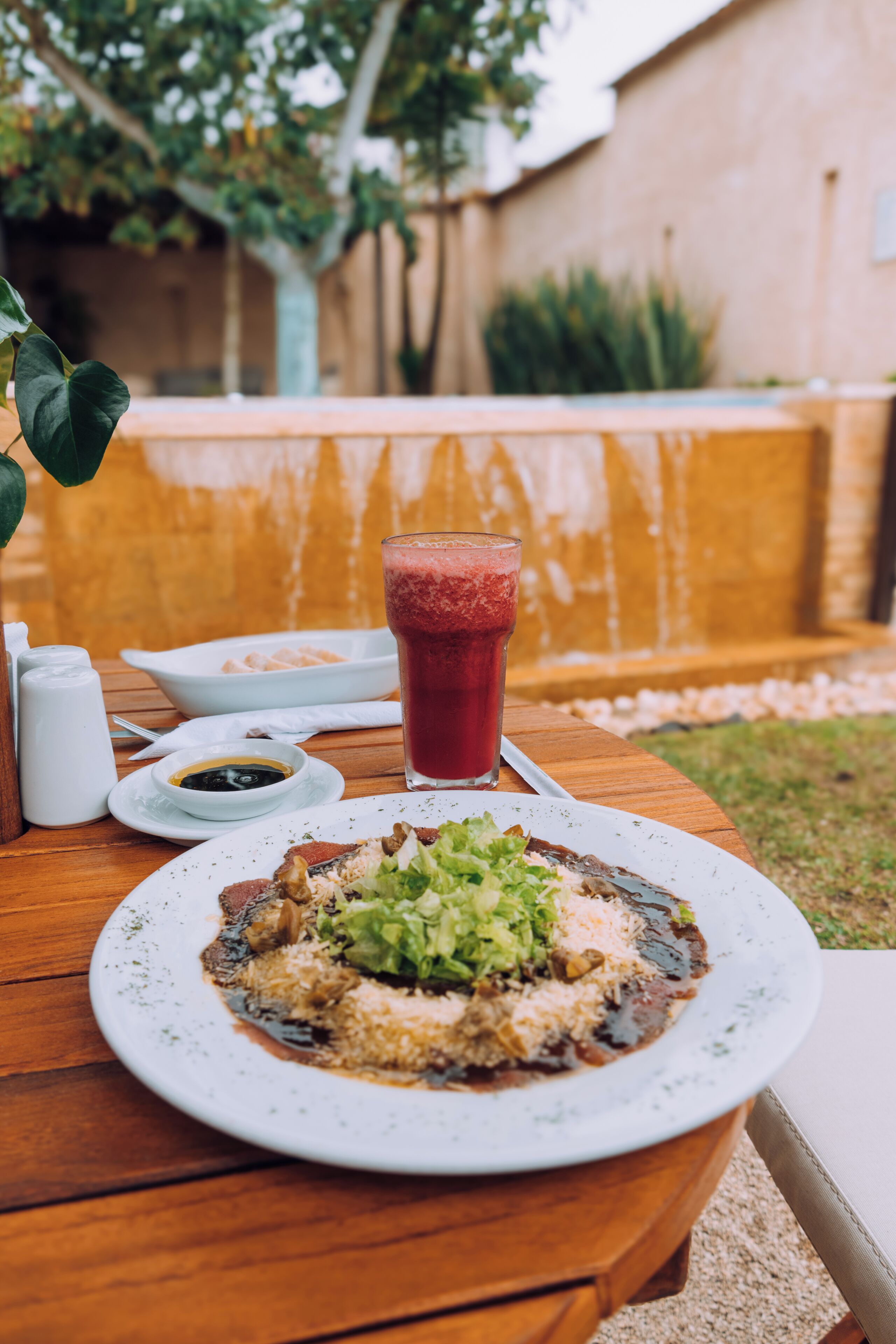 A wooden table with a plate of food and a glass of red drink.