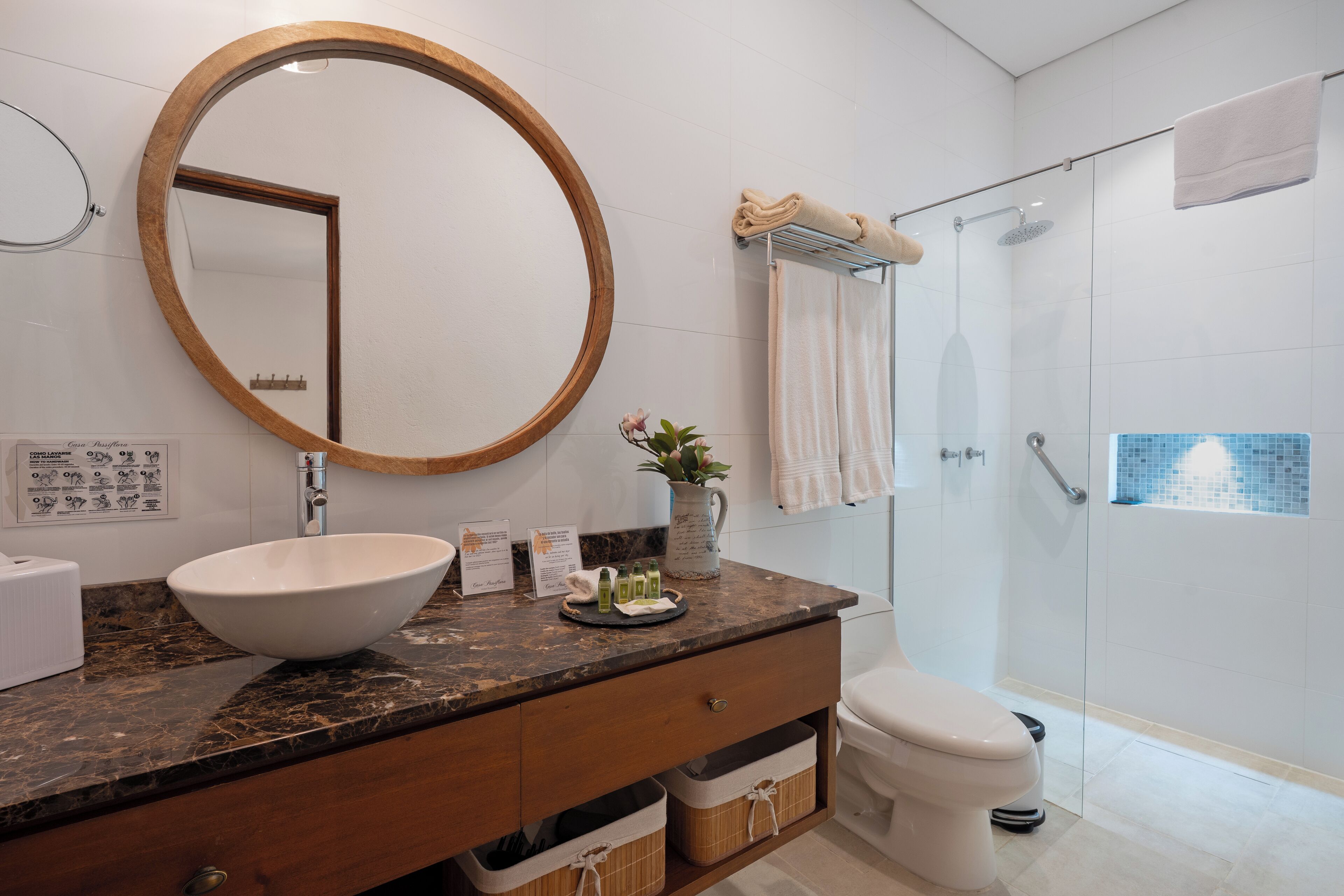 A bathroom with a round mirror, a sink, a toilet, and a shower.