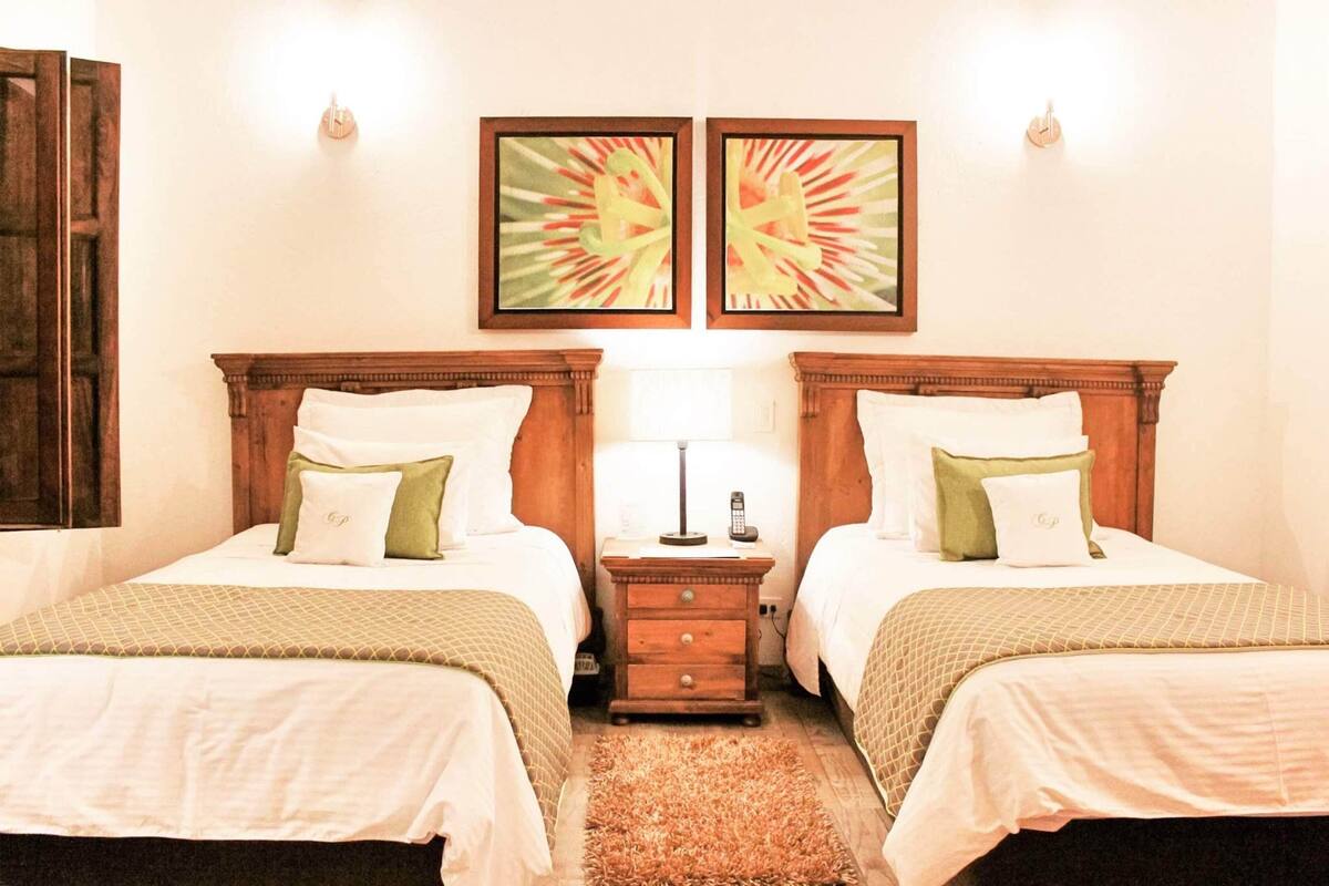 Ein Hotelzimmer mit zwei Betten, einem Nachttisch mit Lampe und zwei gerahmten Bildern an der Wand.