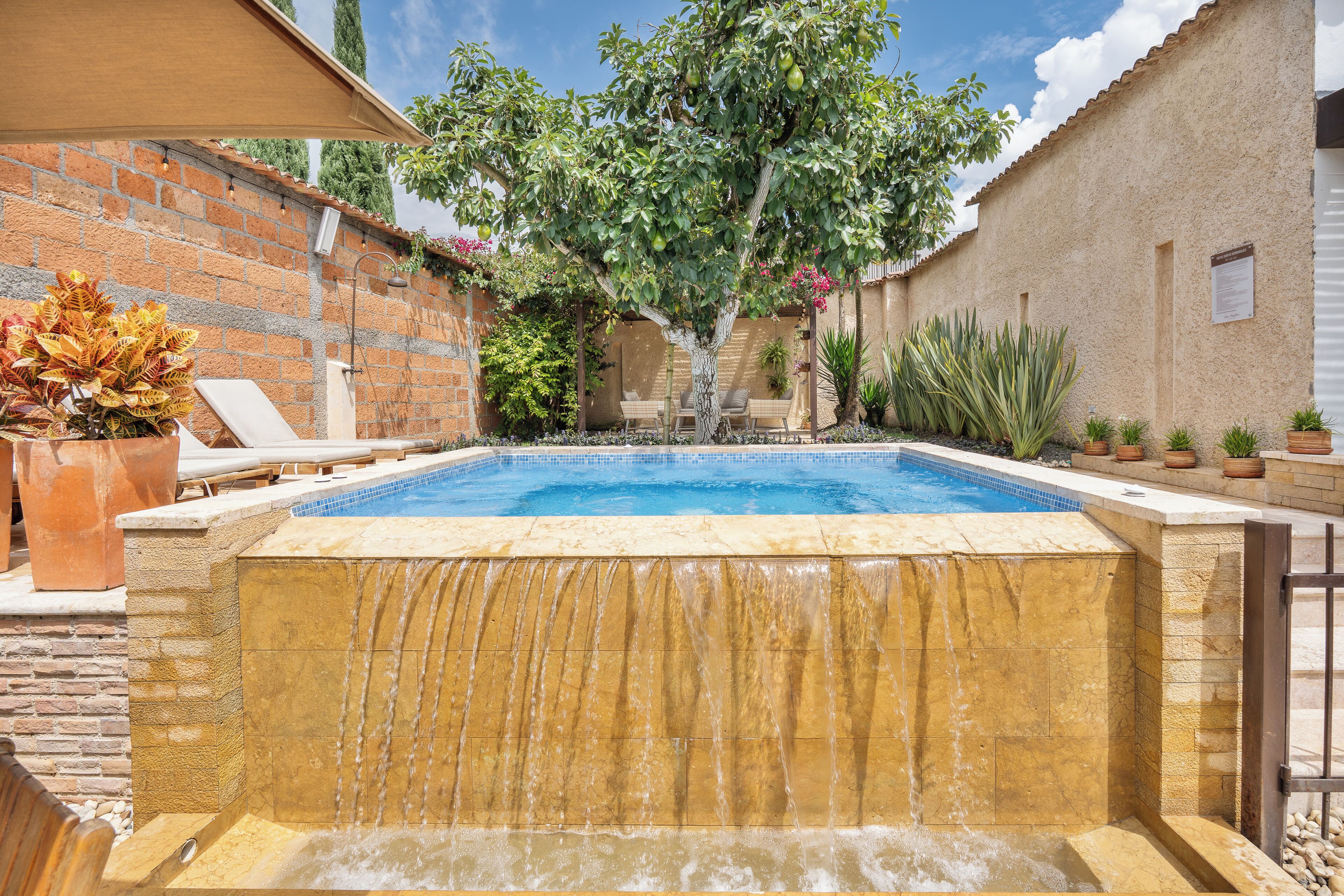 A swimming pool with a waterfall feature, surrounded by a brick wall and potted plants.