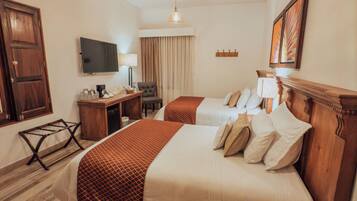 A hotel room with two beds, wooden flooring, a desk with a chair, a television, and a large window with curtains.