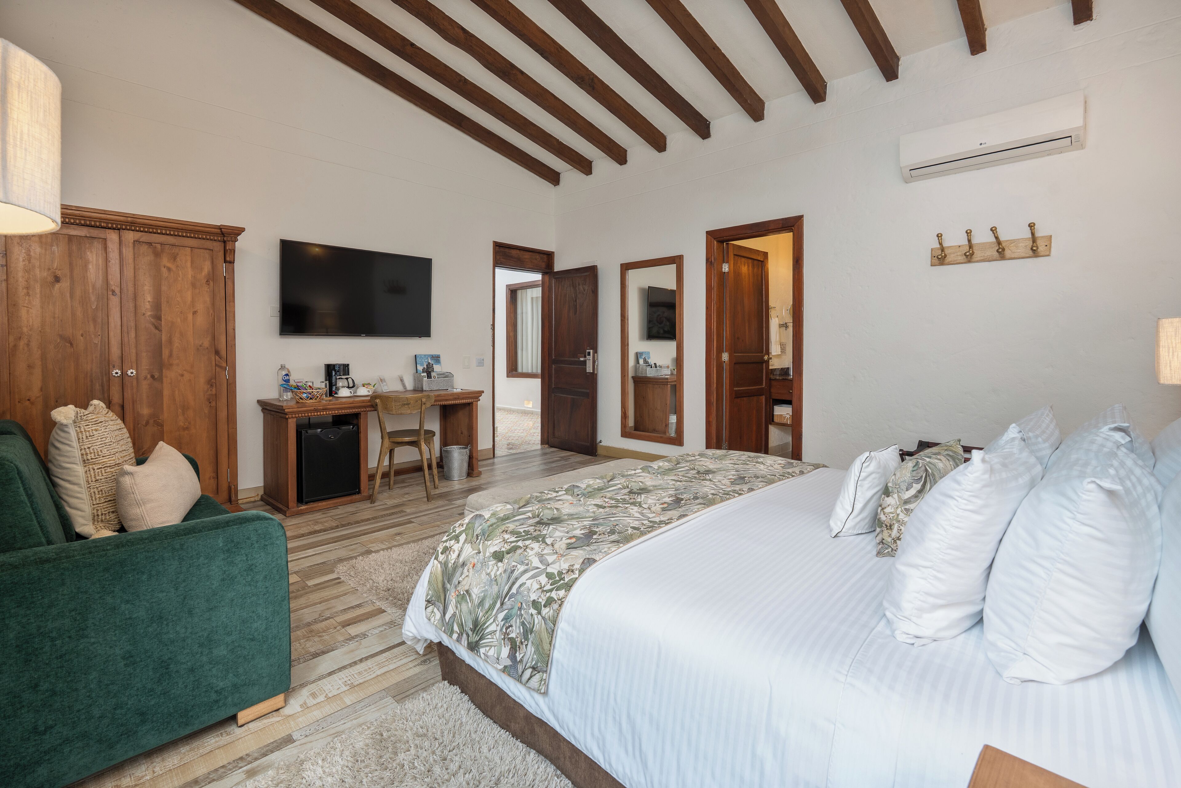 Un dormitorio con una cama grande, un escritorio, un televisor y vigas de madera en el techo.