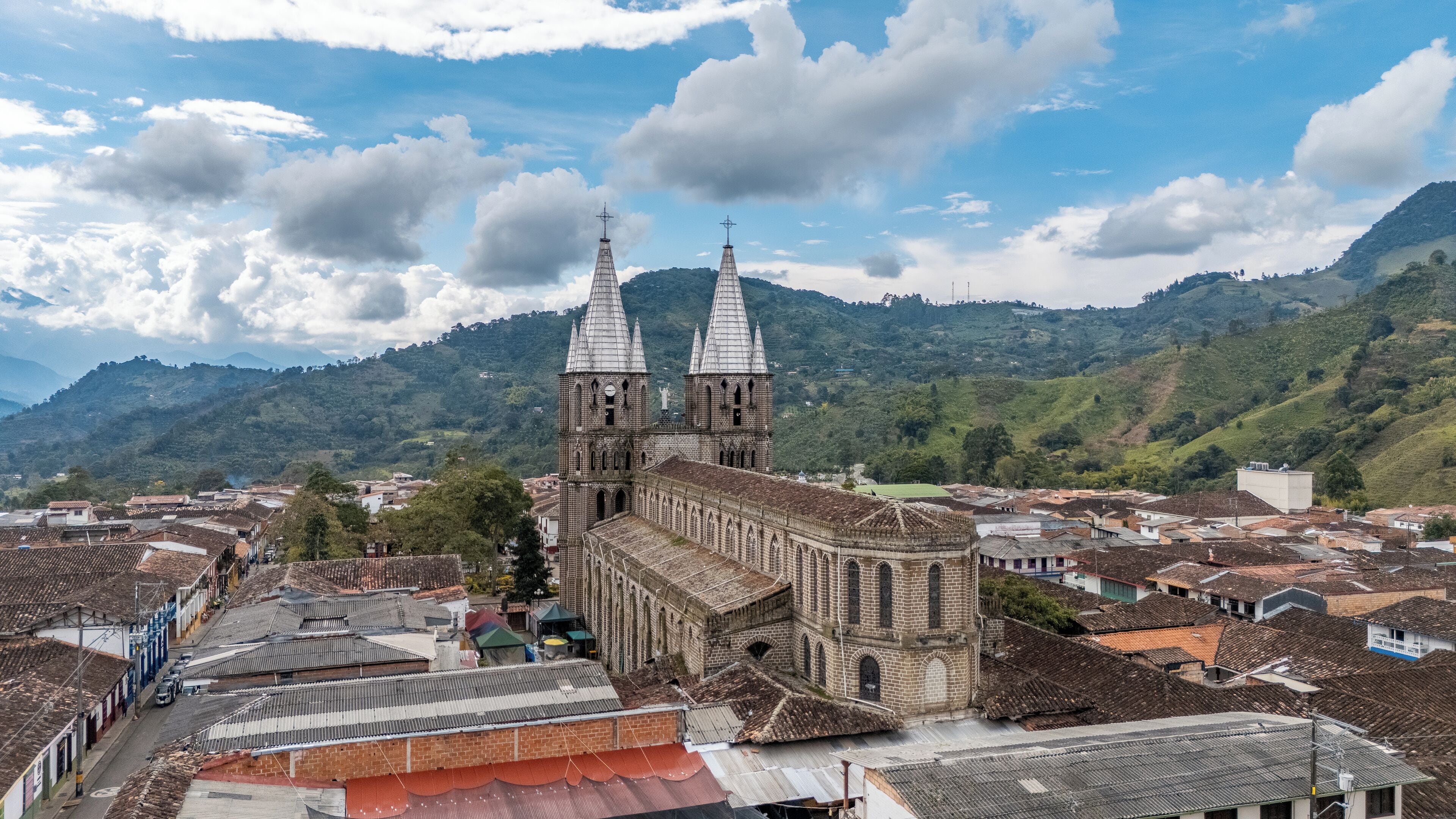 A historic church with two towers and a large bell tower, surrounded by traditional buildings and lush green hills.