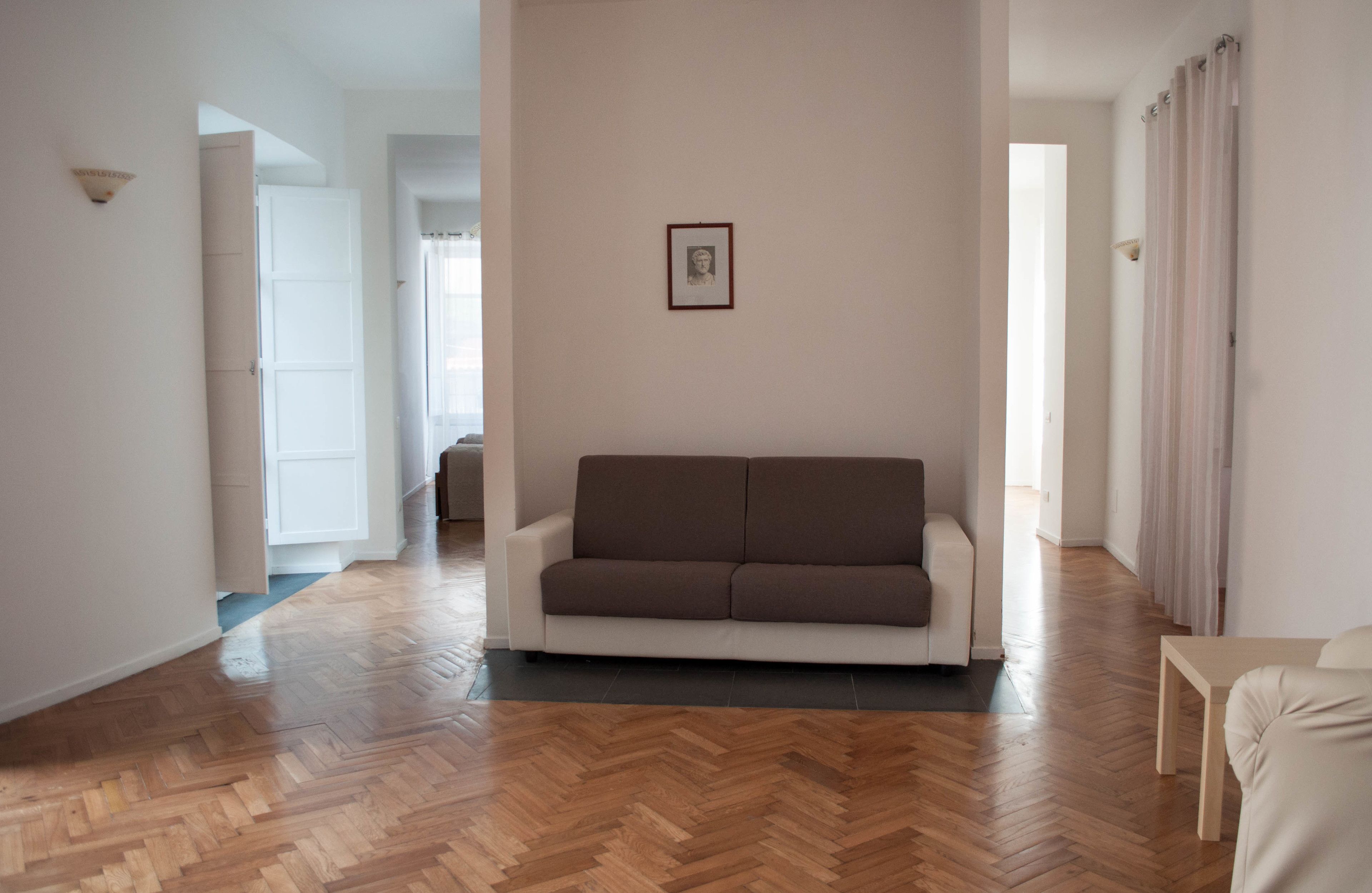 Un ampio soggiorno con pavimento in parquet a spina di pesce, un divano bianco e un quadro appeso al muro.