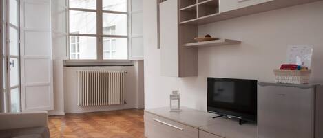 Una sala de estar moderna con piso de madera en diseño de espiga, un sofá, un televisor, un refrigerador y una ventana con vista al exterior.