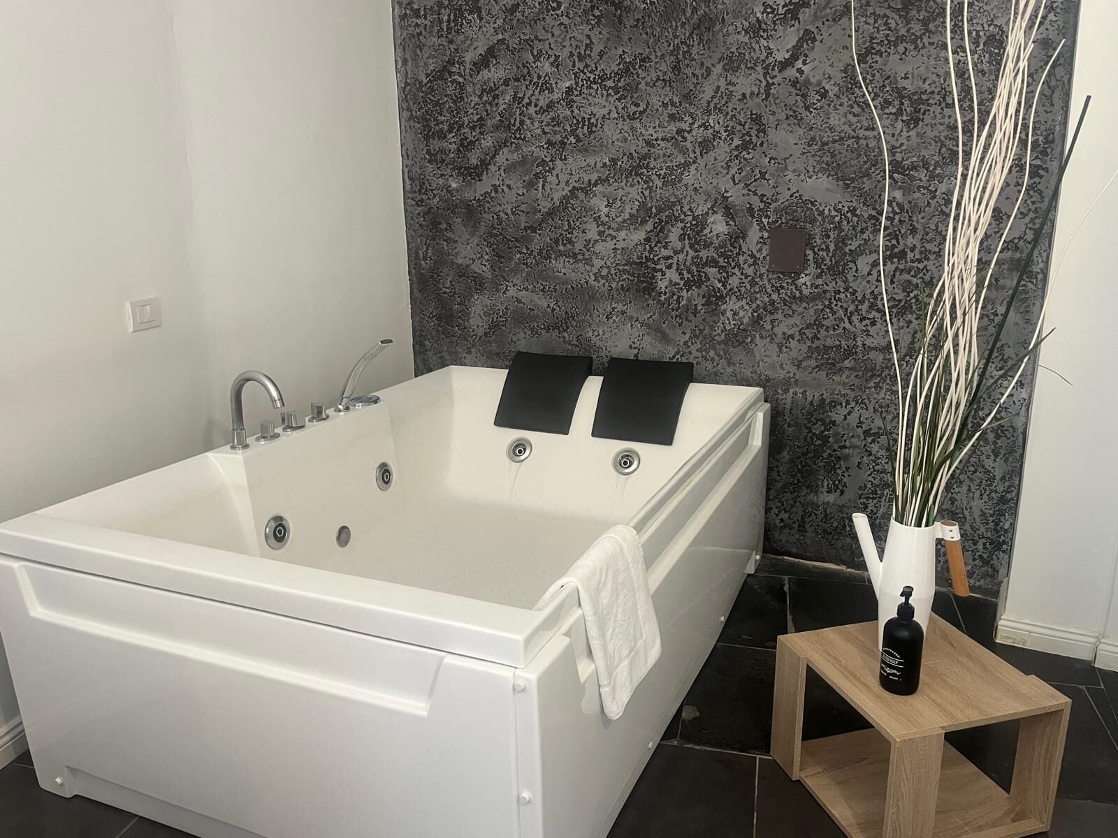 Une salle de bain moderne avec une baignoire sur pieds, une petite table d’appoint en bois et un vase avec des plantes.