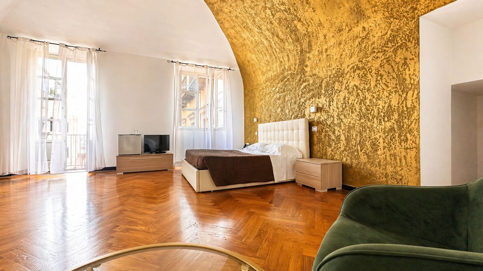 Een slaapkamer met een bed, nachtkastjes, een televisie en een groene stoel.