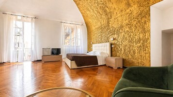 Un dormitorio con cama, mesitas de noche, televisor y una silla verde.
