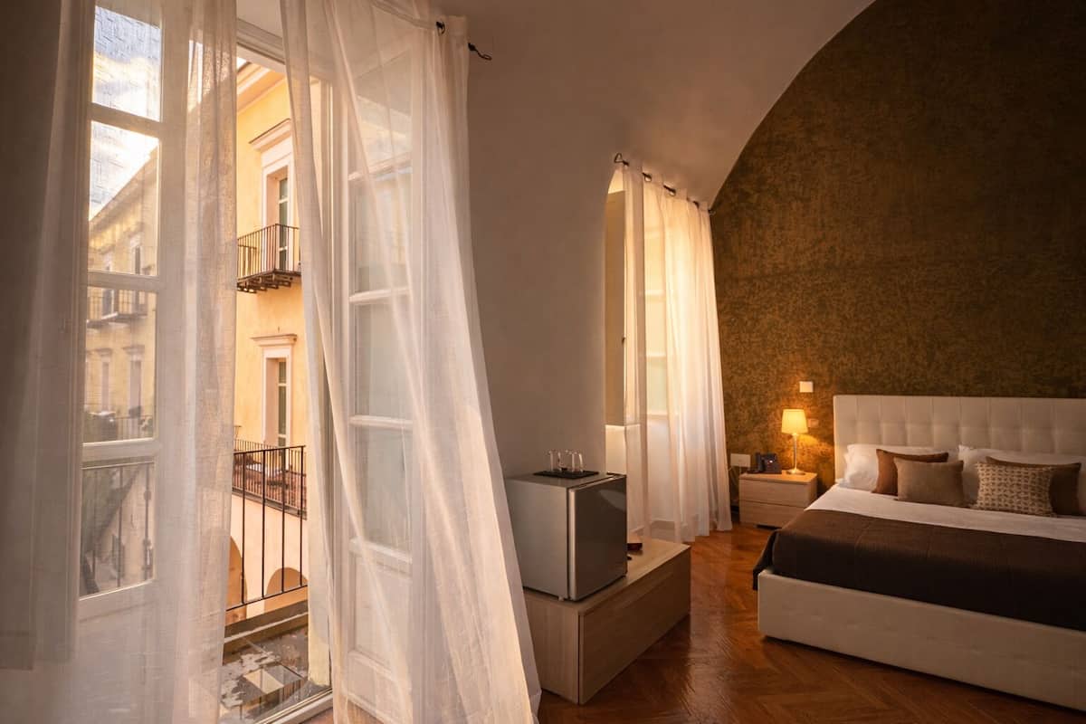 A bedroom with a bed, bedside table, lamp, and a view of the outside balcony.