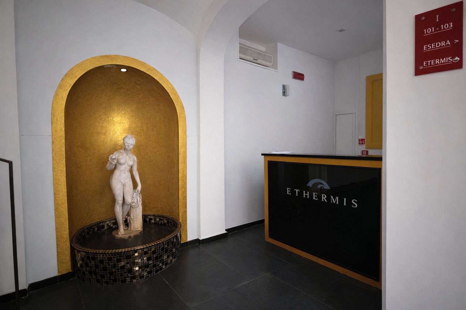 A reception area with a golden archway, a statue, and a reception desk labeled 'ETHERMIS.'