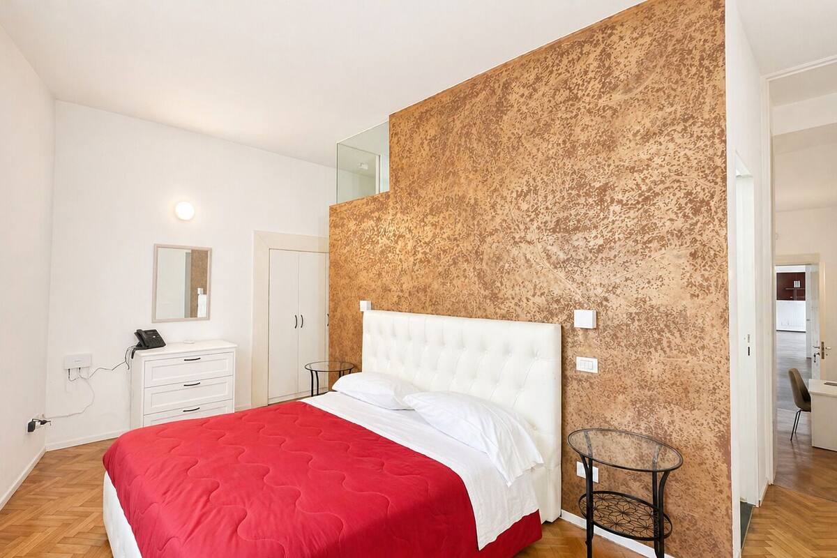 A bedroom with a bed, a dresser, a mirror, and a patterned wall.