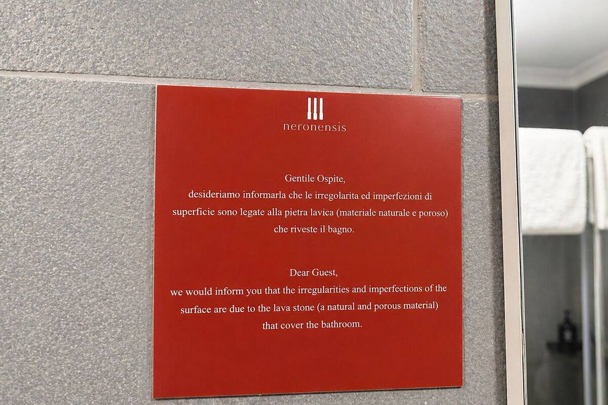 A red informational plaque in a bathroom with a tiled wall and a glass shower enclosure.