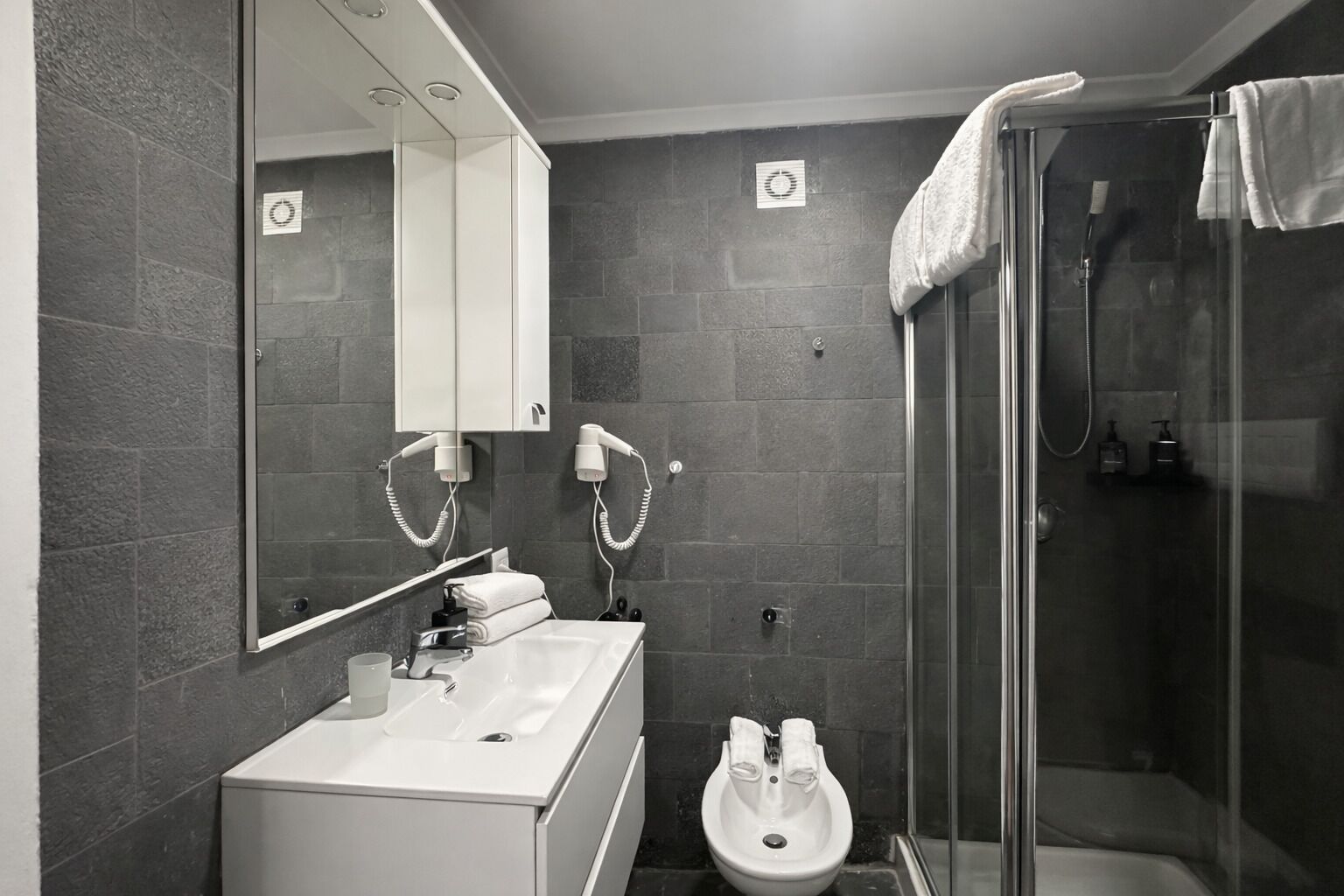 Un baño moderno con un lavabo, espejo y ducha blancos.