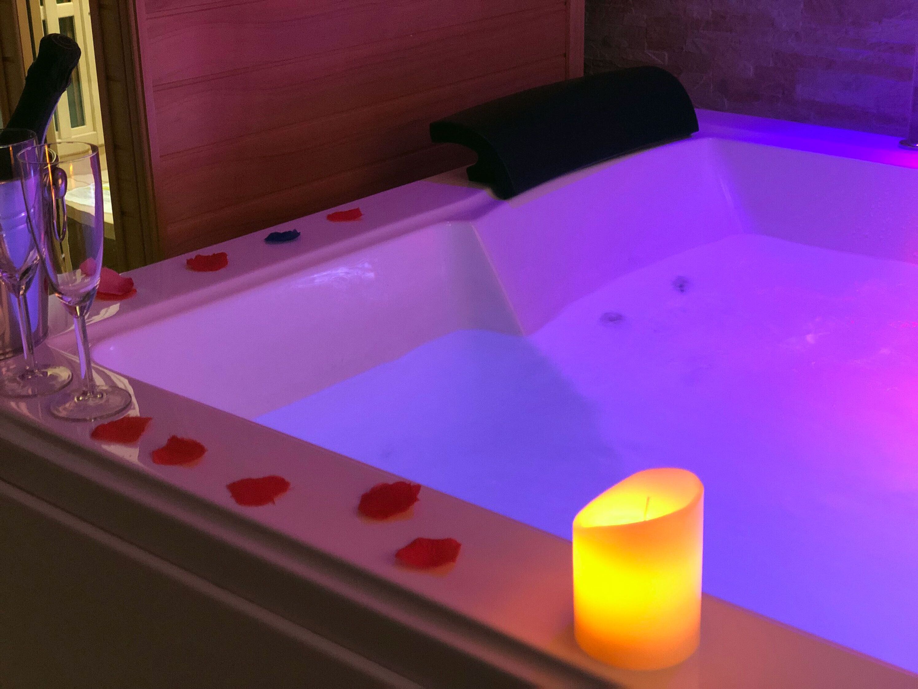 A hot tub with rose petals and a lit candle.