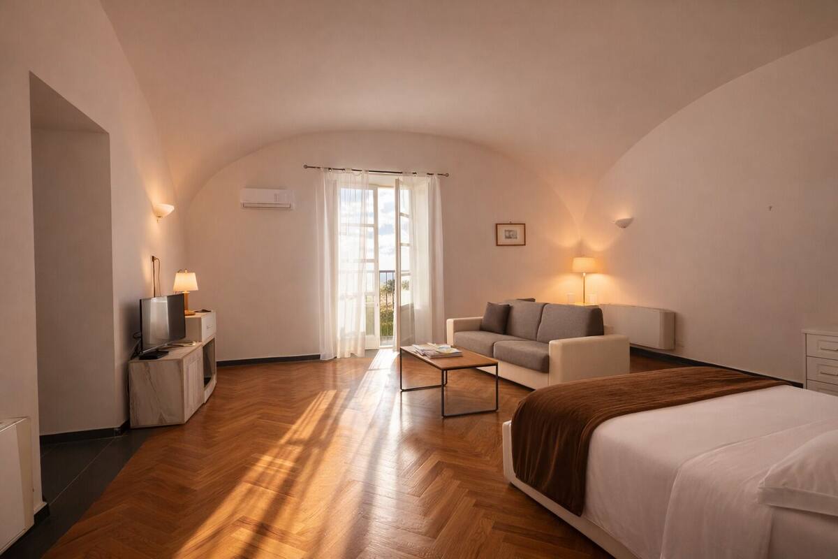 A hotel room with a bed, a sofa, a TV, a coffee table, and a desk with a lamp.